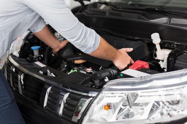 An expert from an auto repair shop working on a car’s battery and engine